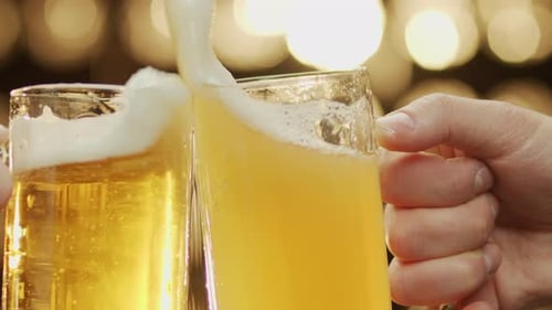 Gros plan d'une clinique de bière à deux mains renversant de la bière sur fond de bokeh