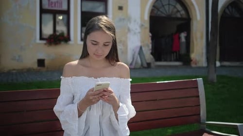 Woman on Bench Using Mobile Phone Outside