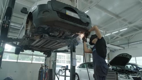 Mechanic Welding Car Underside in Auto Shop