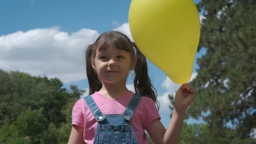 Smiling Girl Holding Yellow Balloon in Park