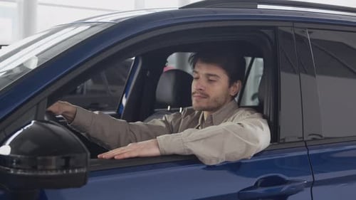Young Dreamy Guy Sitting in New Car at Dealership Salon Enjoying His Purchase and Showing Thumb Up