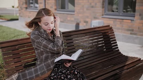 a girl reads a book on a street bench