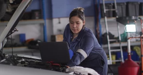 Female mechanic using laptop and inspecting the car at a car service station
