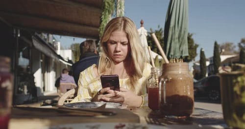 Woman Using Smartphone As She Waits on Restaurant Table Outside on a Sunny Day