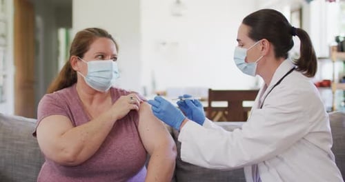 Caucasian woman and female doctor wearing face masks, vaccinating