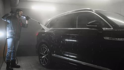 Hombre lavando un coche negro con un chorro de agua a alta presión en un garaje