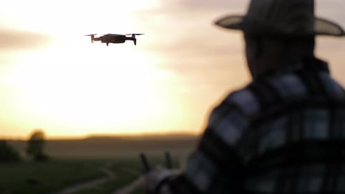 Man Operates Drone in Field at Sunset
