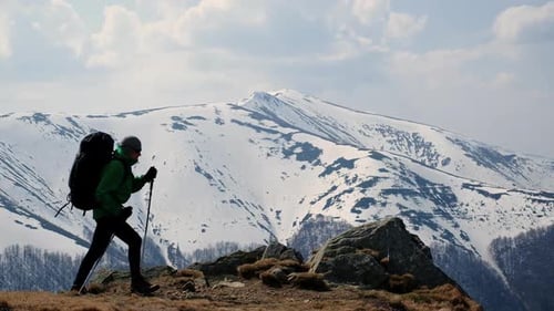 Hiker with Backpack Walking Toward Snowy Mountains