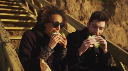 Couple Eating Sandwiches on Beach Stairs at Sunset