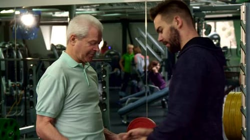 Senior Man Lifts Weights With Trainer at Gym