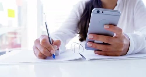 Woman writing notes while using her smartphone