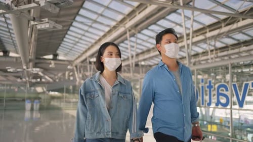 Man and woman passengers wearing face mask walking in airport terminal to boarding gate.