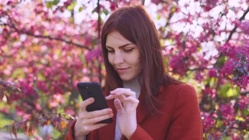 Attraktive junge rothaarige Frau benutzt Smartphone im Park bei Sonnenuntergang