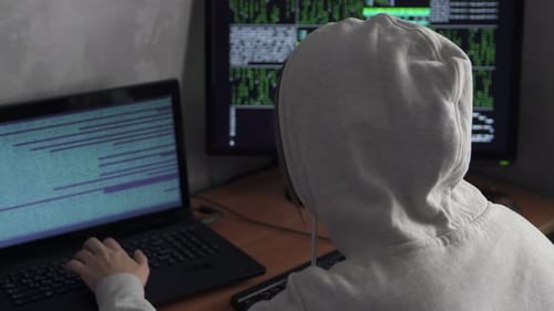 O hacker se senta de costas contra o fundo das telas dos computadores em funcionamento.