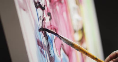 Gros plan de la main d'un artiste masculin peignant avec un pinceau sur toile dans un studio d'art