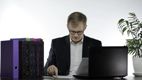 Businessman Working in Office. Analyzing Paperwork and Work on Laptop