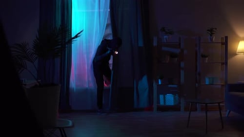 Figure with Flashlight Searches in Dark Room at Night