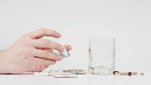 Adult Taking Pills with Water on White Table