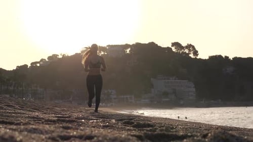 Sporty Female Running Along Sandy Beach at Sunrise