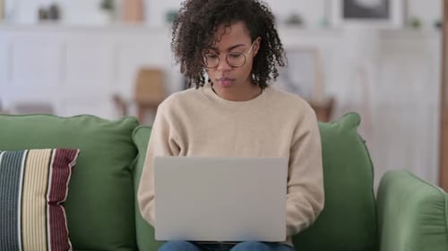 African Woman with Laptop Reacting to Failure on Sofa