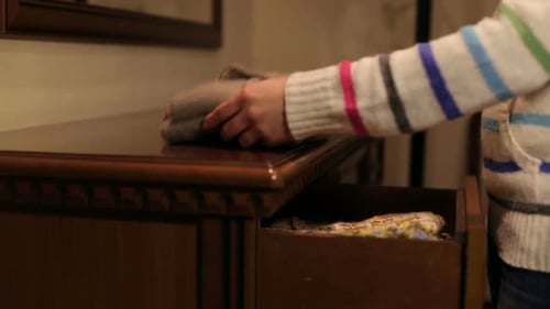 Woman Unfolds a Sweater on a Dresser