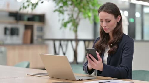 Woman Using Laptop and Phone in Modern Office