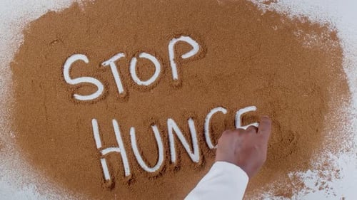 Hand Writes "Stop Hunger" in Brown Powder