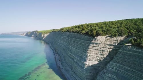 Aerial of High Steep Cliffs Covered with Pine Trees and Wild Pebble Beach with Turquoise Sea Water