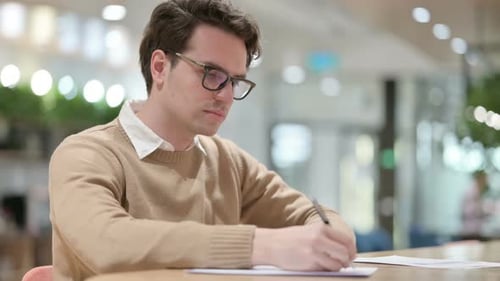Young Male Designer Writing on Paper in Office