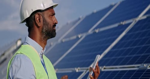 Nahaufnahme eines männlichen Arbeiters gemischter Abstammung, der auf den Tablet-Bildschirm und das Solarpanel schaut. Mann mit hartem Helm und