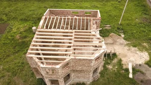 Luftaufnahme eines Backsteinhauses mit im Bau befindlichem Holzdeckenrahmen.