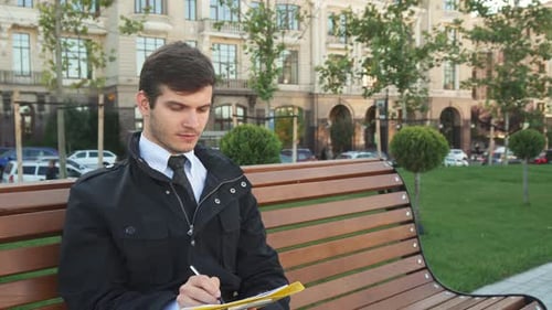 Young Man Writing Notes on Park Bench