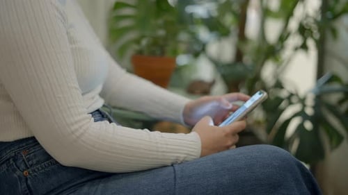 Unrecognizable Woman Using a Mobile Phone While Sitting on a Chair Side View