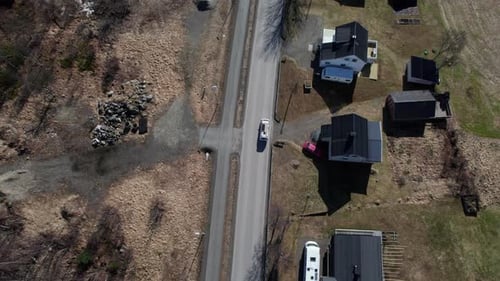 Aerial birds eyes view of a van driving on road past houses in the fall or spring with leafless tree