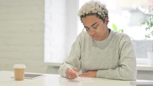 African Woman Thinking While Writing on Paper in Office