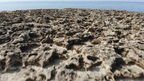 A low-level aerial drone shot flies backward across the Salt Pans of Gozo Island in Malta.