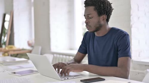 Young African Designer Working on Laptop in Loft Office