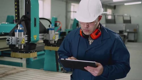 A Male Factory Worker Uses a Tablet in the Workshop