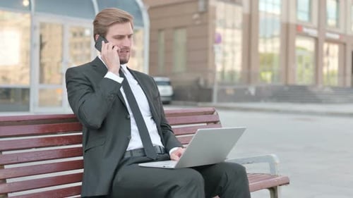 Businessman Talking on Phone With Laptop on Bench