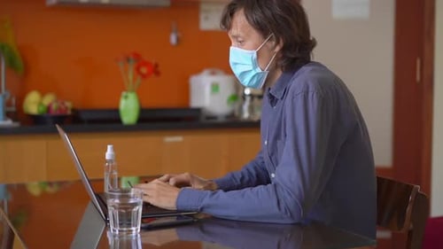 A Young Man Wearing a Face Mask Works From Home During Coronavirus Self-isolation