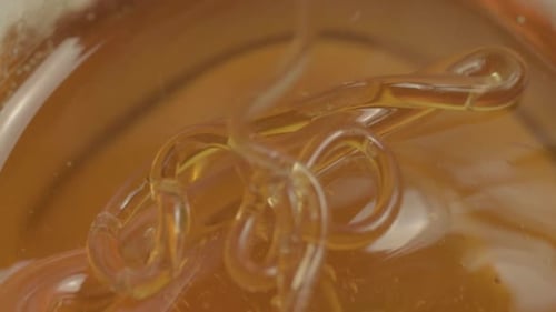 Clear golden runny honey dripping into a jar macro