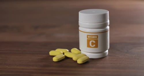 Vitamin C Bottle and Yellow Tablets on Wood