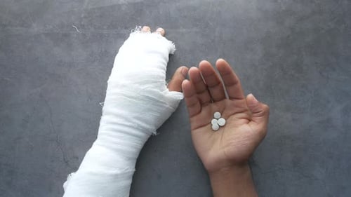 Verletzte schmerzende Hand mit Bandage und medizinischen Pillen
