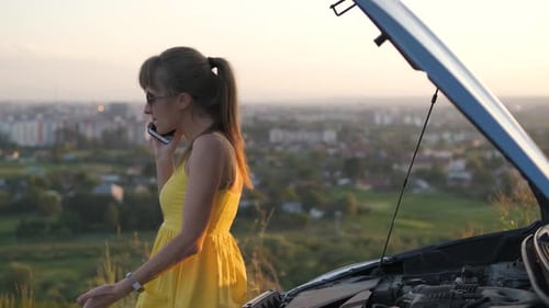 Young Woman Driver Talking on Mobile Phone Standing Near Her Car with Open Hood Having Motor Problem