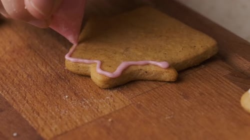 Woman Decorates a Gingerbread in the Shape of House on the Wooden Desk with Icing