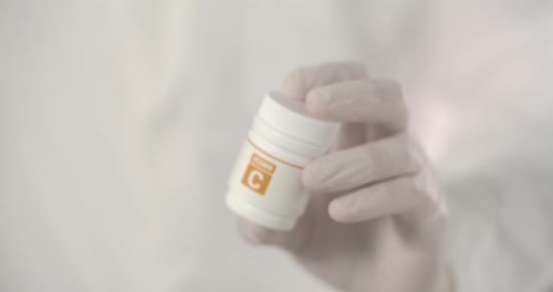 Gloved Hand Holding Vitamin C Container