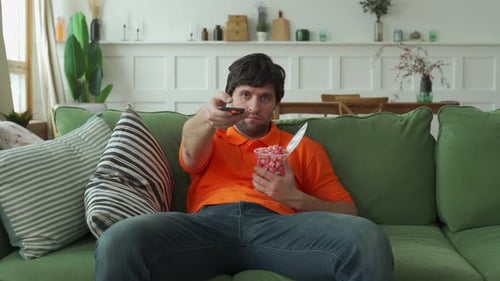 Man Relaxing on Couch, Watching TV and Eating Popcorn