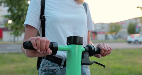 A woman is holding onto her electric scooter on the city street.
