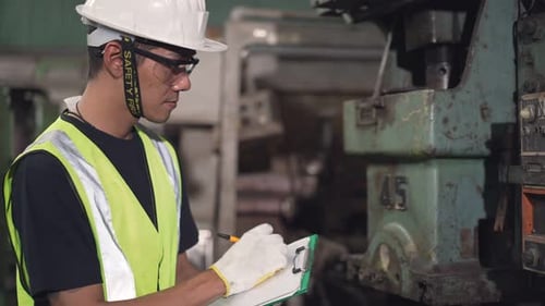 Asian male factory worker writing on checklist clipboard in the factory