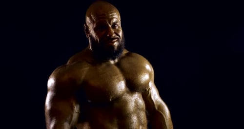 Naked Bodybuilder Man Is Standing in Darkness in Studio, Showing Muscles of Torso